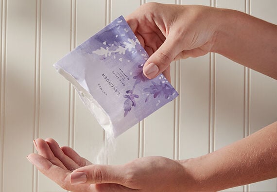Thymes Lavender Bath Salts being poured from envelop into hand and bath
